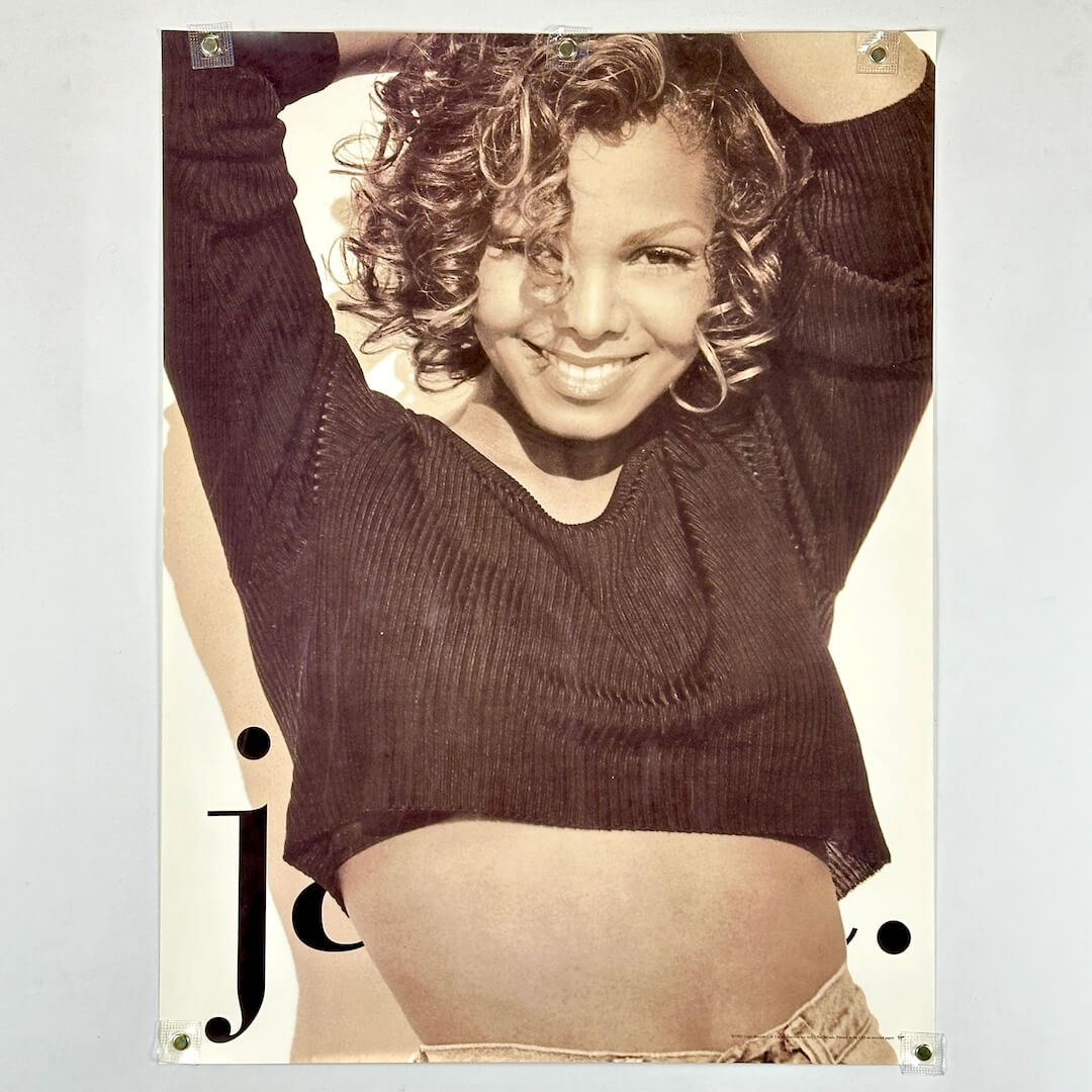 Poster of Janet Jackson wearing a crop top with hands above her head, "J" in bottom left corner.