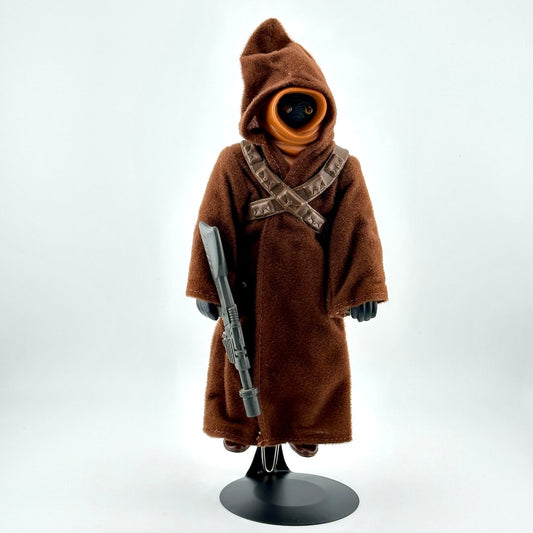 8 inch Jawa doll/figure in brown robe with gun held aloft by doll stand. 