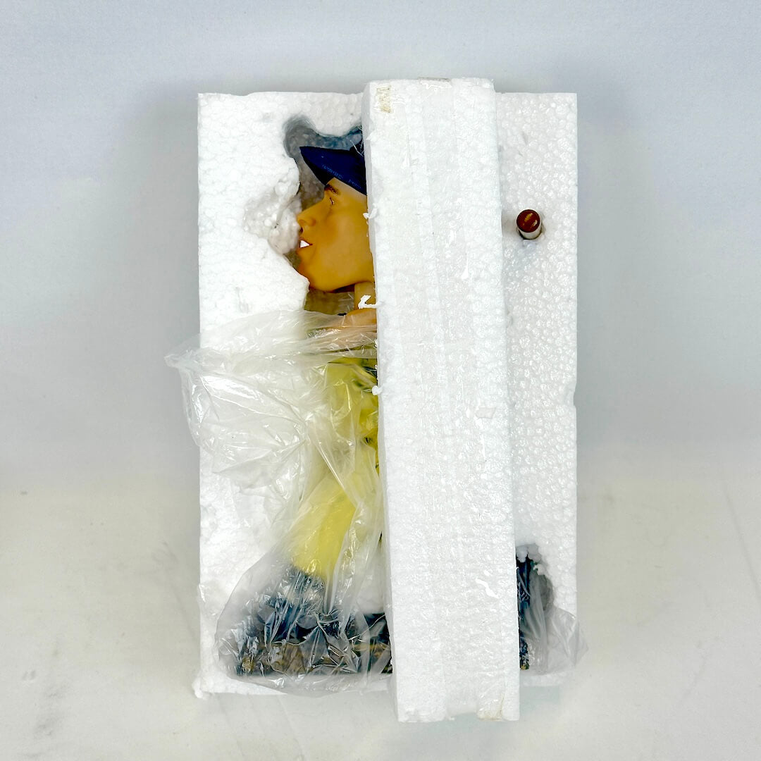 A packaged collectible figurine partially wrapped in white foam and clear plastic.