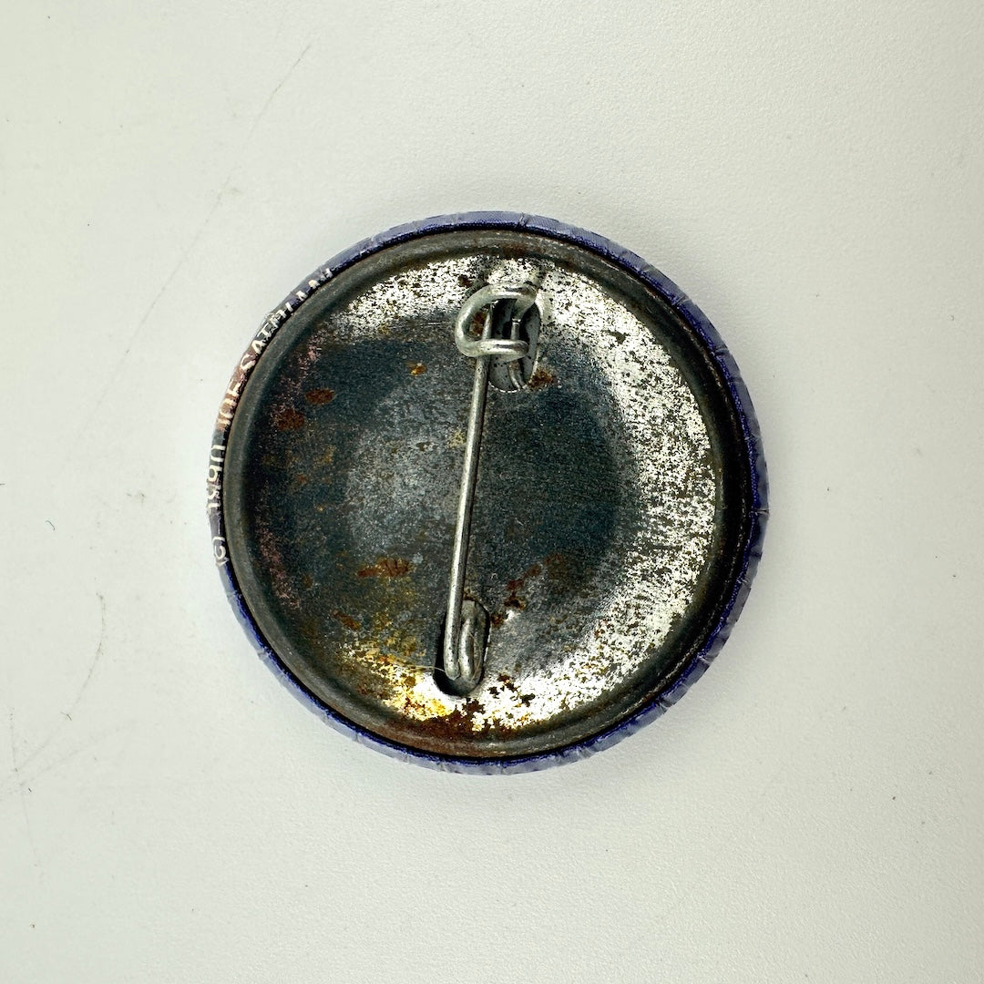 The back of a round pinback button badge, showing a tarnished silver metal safety pin clasp.