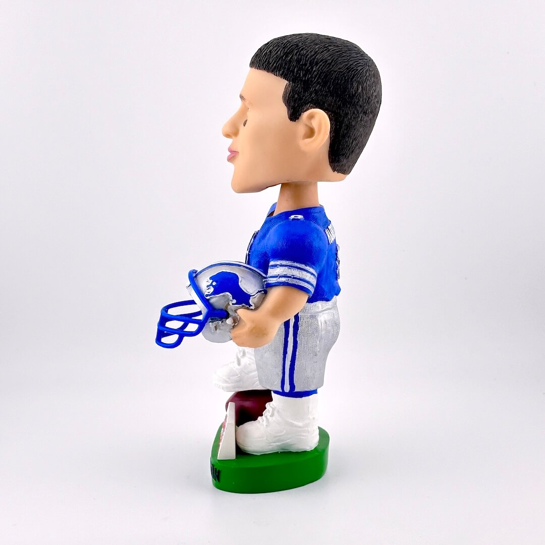 Side view of football player bobblehead in blue jersey holding helmet against white background. 