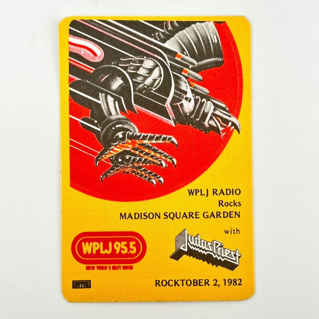 Yellow rectangular backstage pass with iron eagle illustration above event details in black text. 'Judas Priest' branding visible. 