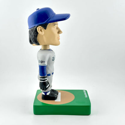 Baseball bobblehead figure with blue cap and white uniform on a green base