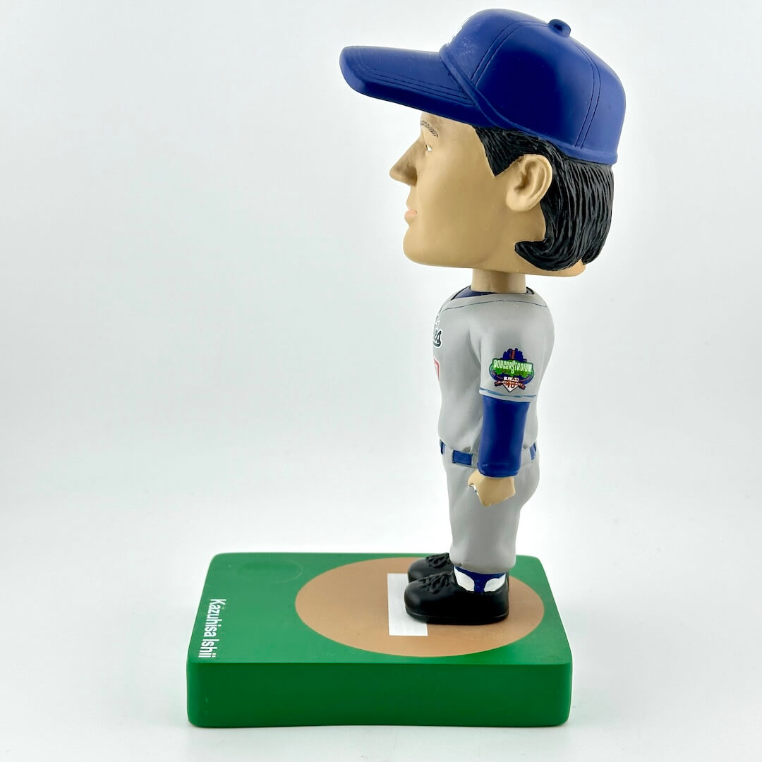 Bobblehead figure of a baseball player in a blue and gray uniform on a green base with a white background