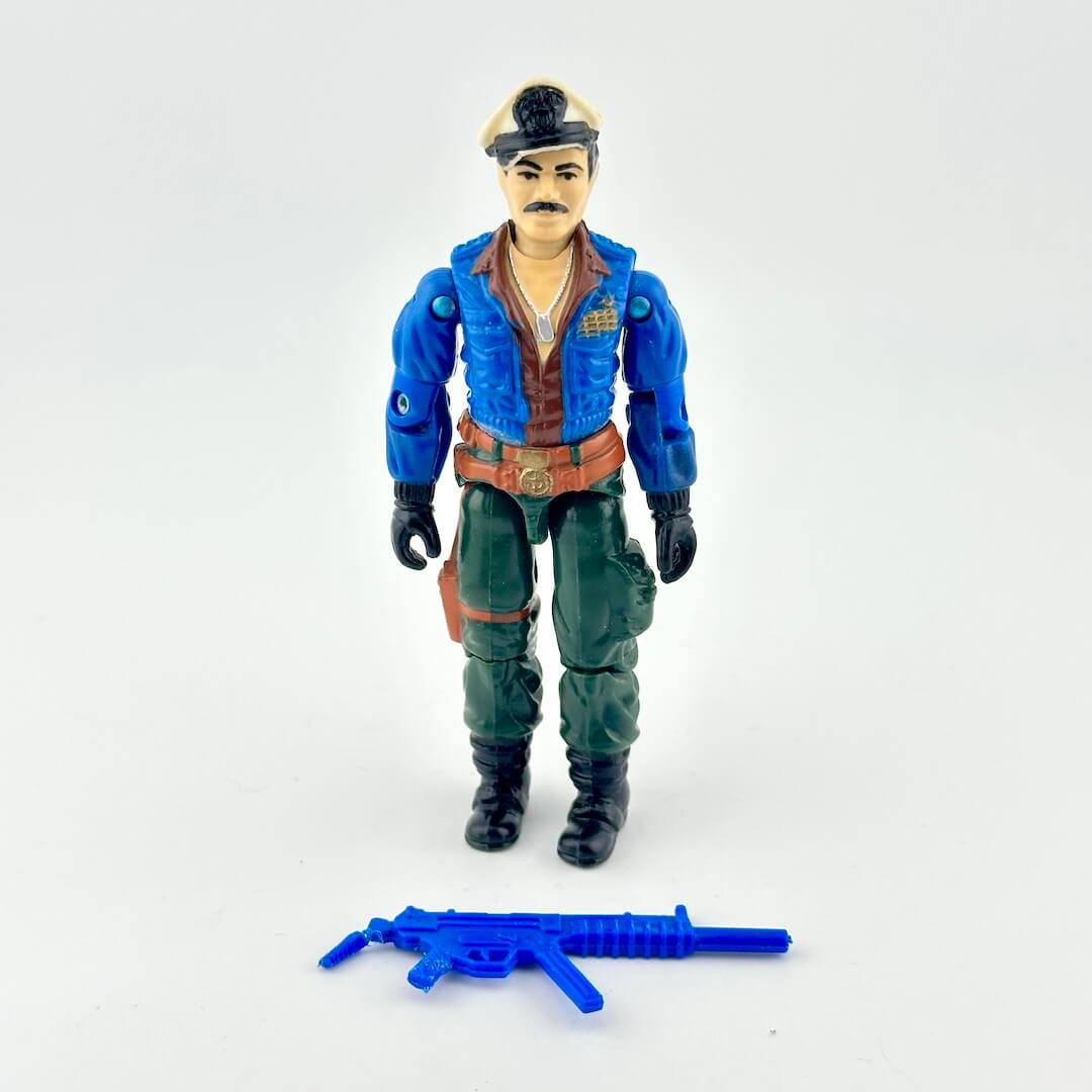 GI Joe action figure with blue jacket, green pants and white hat, pictured with blue accessory on white background.