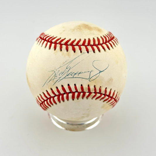 A signed baseball with red stitching, featuring a blue ink signature on neutral background. 