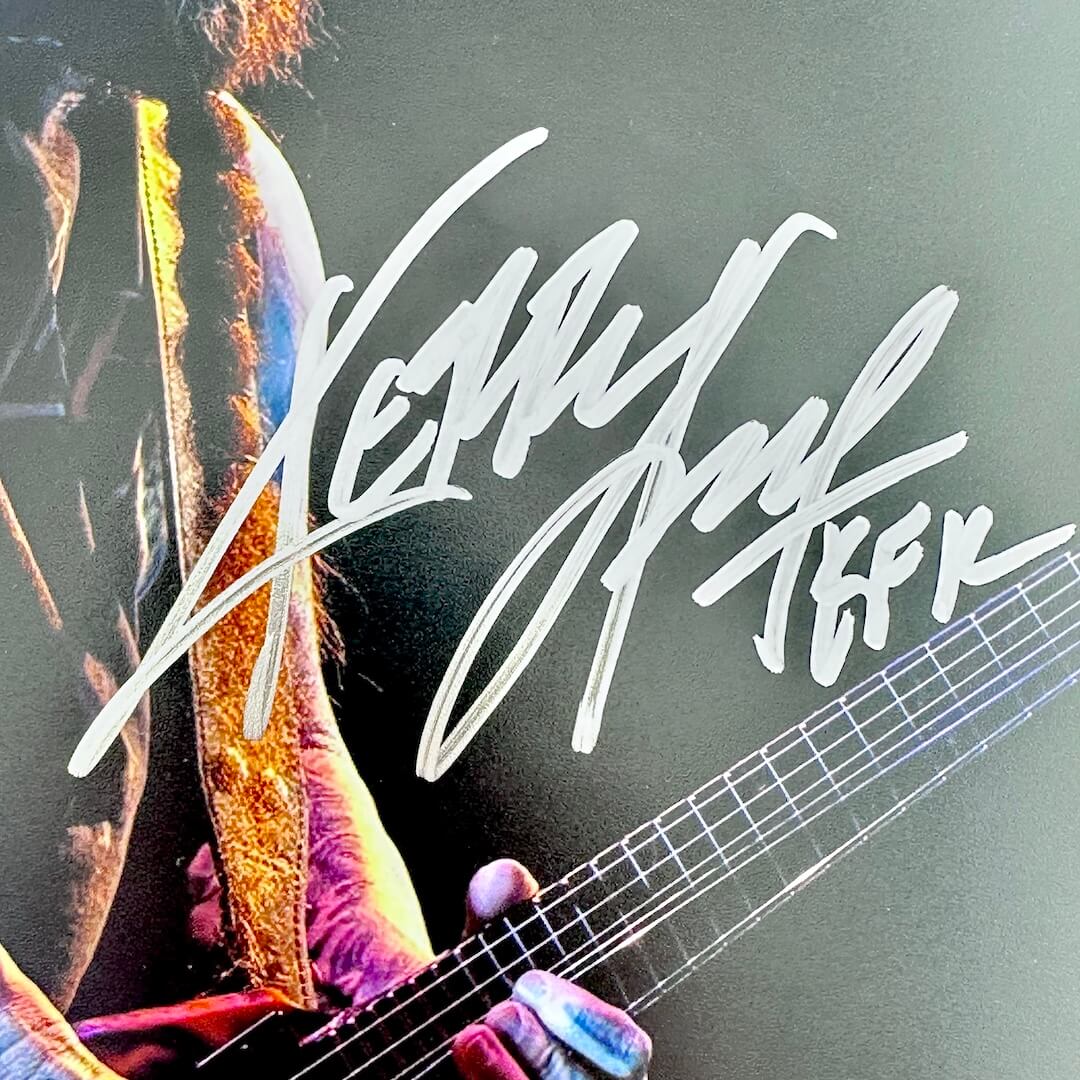 Close-up of a person playing guitar with a signature overlay on a dark background