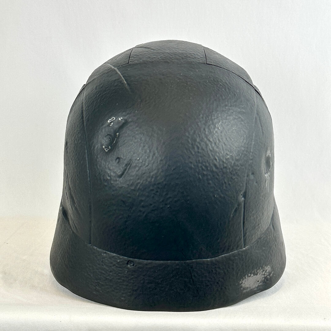 A black textured helmet with simulated scratches, dents, and wear, photographed against a plain white background.