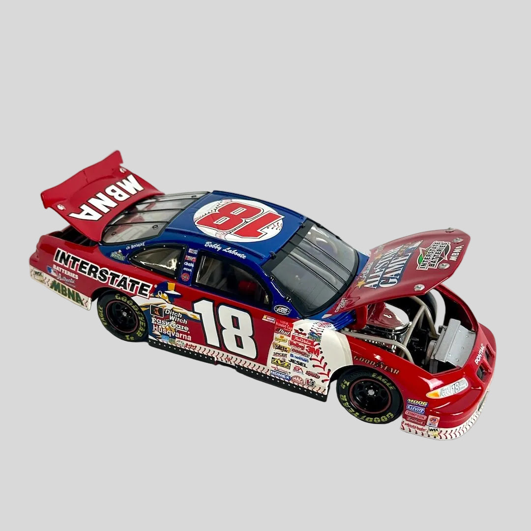 A diecast model race car with an open hood, featuring a red, white, and blue NASCAR livery with the number 18.