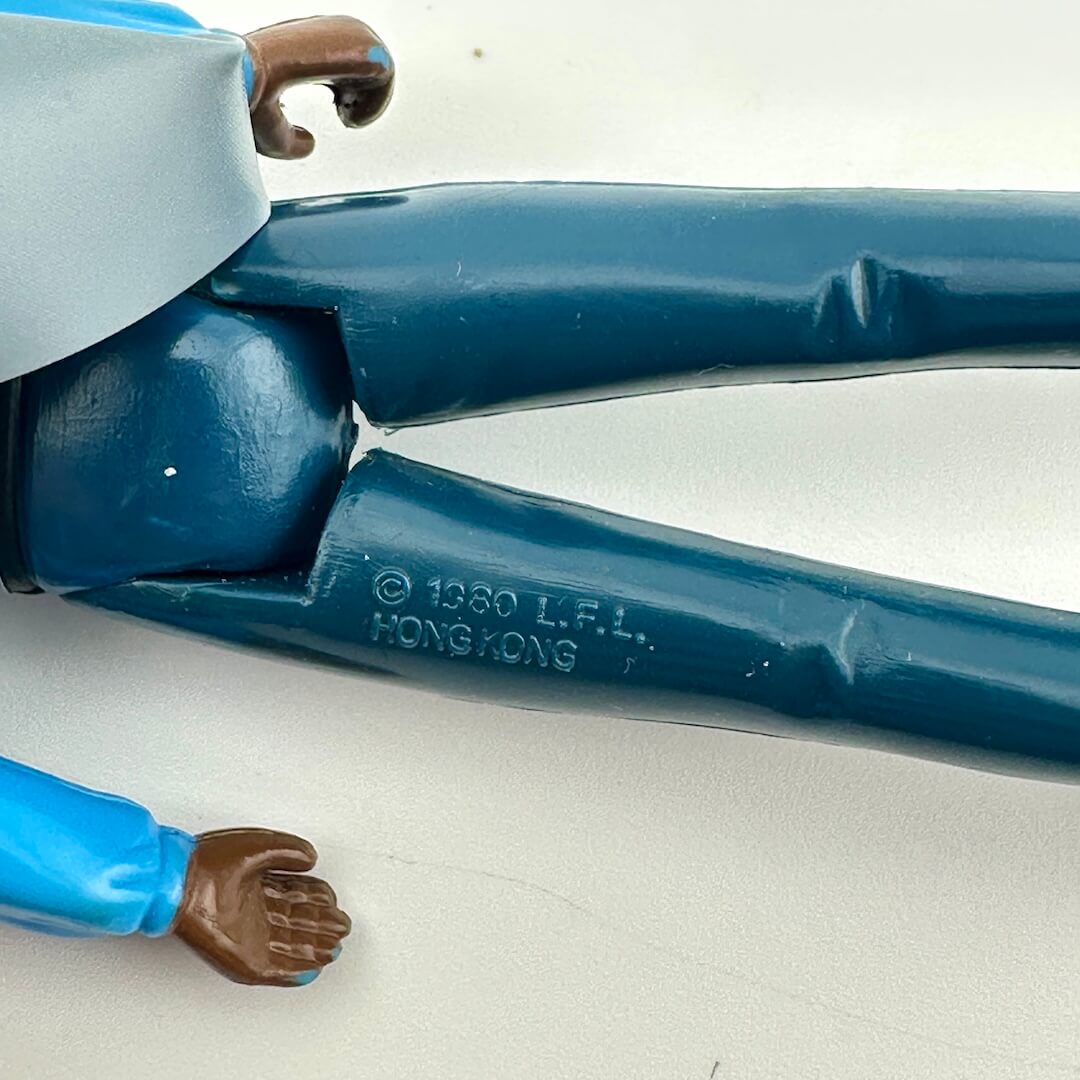 Close-up of a vintage plastic action figure leg joint, showing the blue painted plastic with a molded '© 1980 L.F.