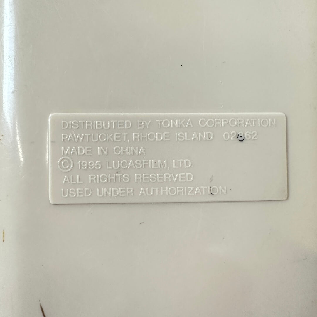 A close-up of a white plastic label with embossed text showing distribution details by Tonka Corporation.