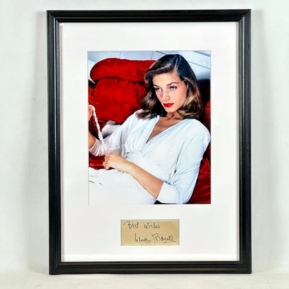 A framed vintage photograph of actress Lauren Bacall, signed at the bottom. The print is matted in white and enclosed in a black frame. 