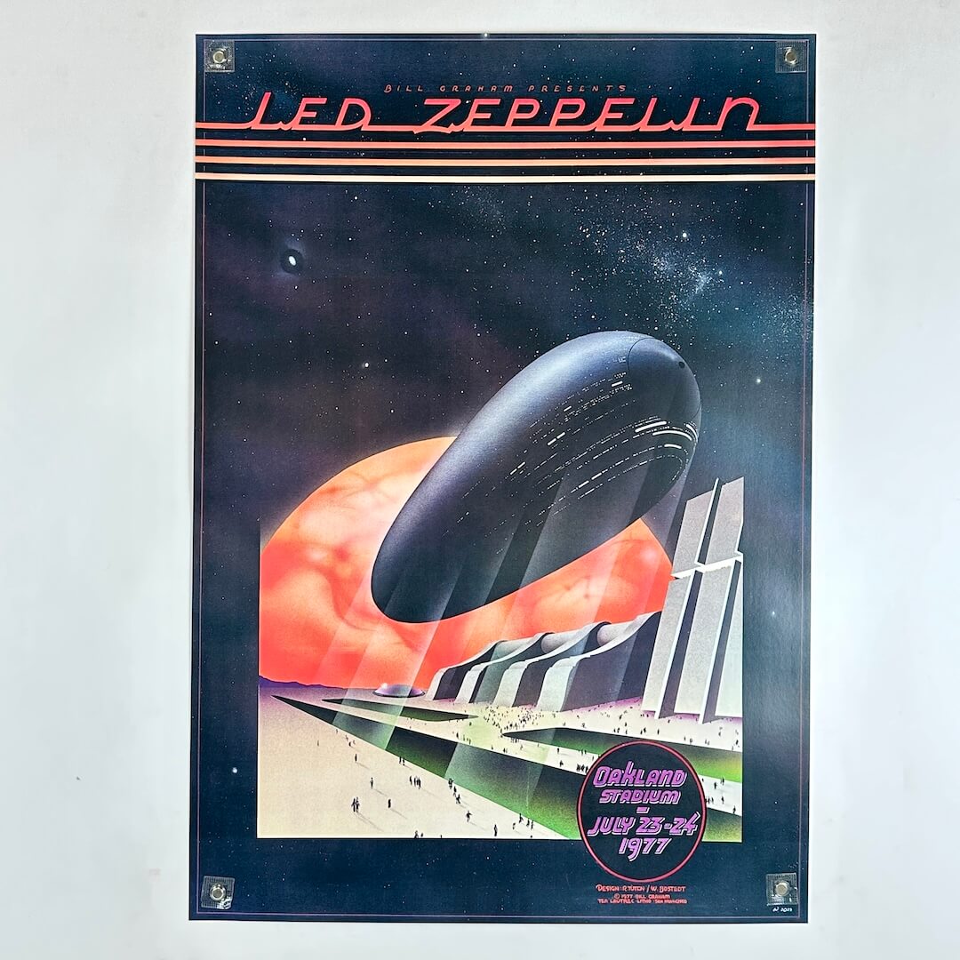 A vintage LED Zeppelin concert poster from Oakland, California, dated July 23-24, 1977 held up by magnets on light surface. 
