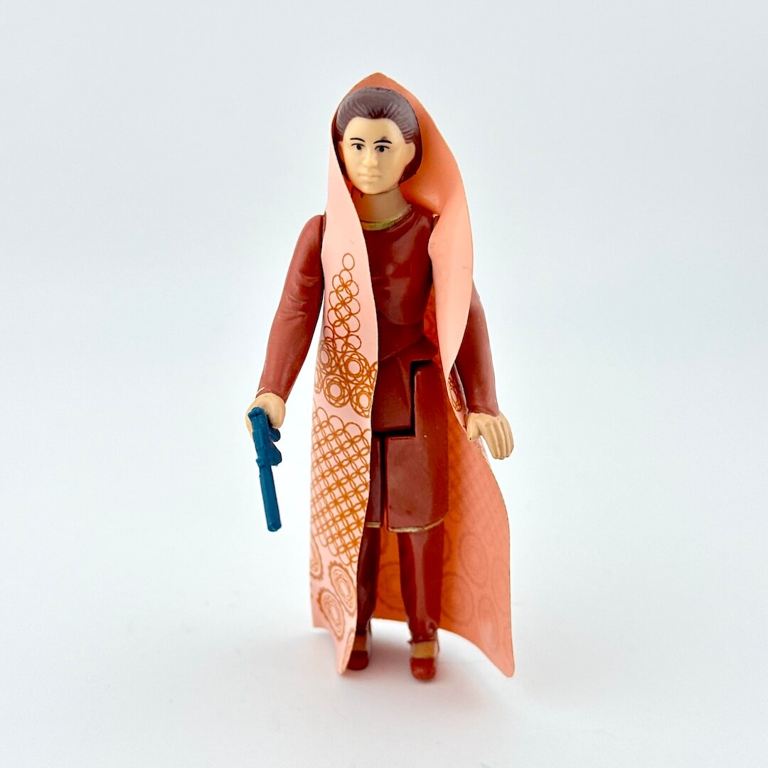 Toy figure of a character with a long brown robe and a blue weapon on a white background