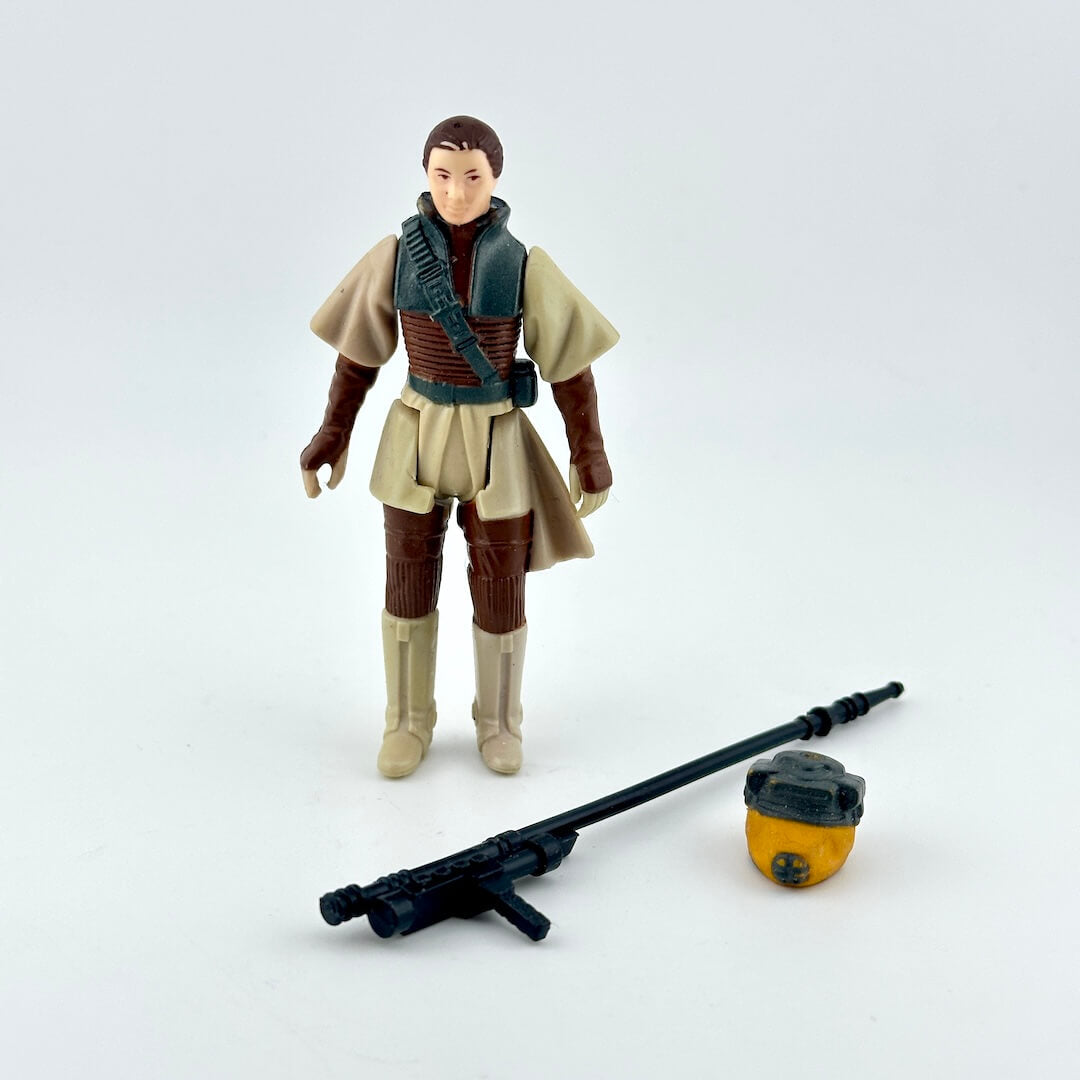 A Star Wars action figure  standing next to a black blaster and a small yellow-and-black helmet.