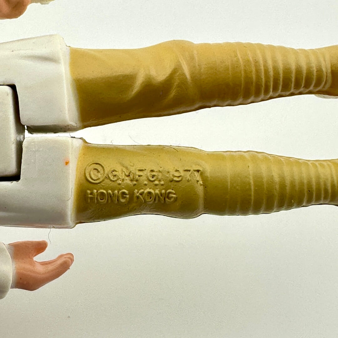 Close-up of back of figure's legs with 'G.M.F.C. 1977 Hong Kong' branding on a white background.
