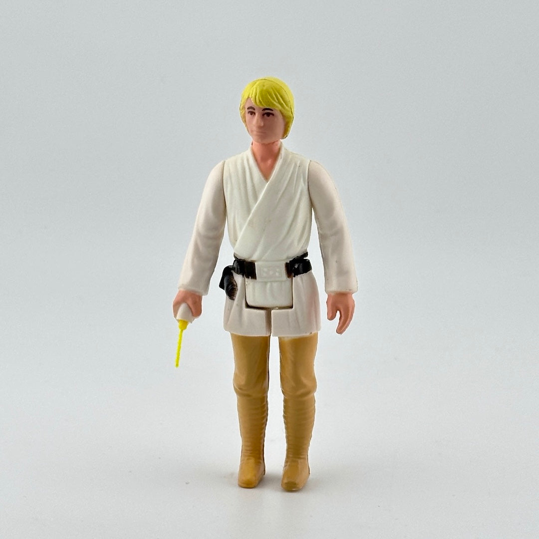 White male action figure with yellow hair in white shirt, black belt & tan pants, yellow lightsaber emerging from right hand.