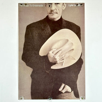 Poster of a man holding a cowboy hat with text 'The Road To Ensenada' and 'Lyle Lovett'.