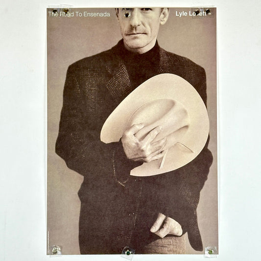 Poster of a man holding a cowboy hat with text 'The Road To Ensenada' and 'Lyle Lovett'.