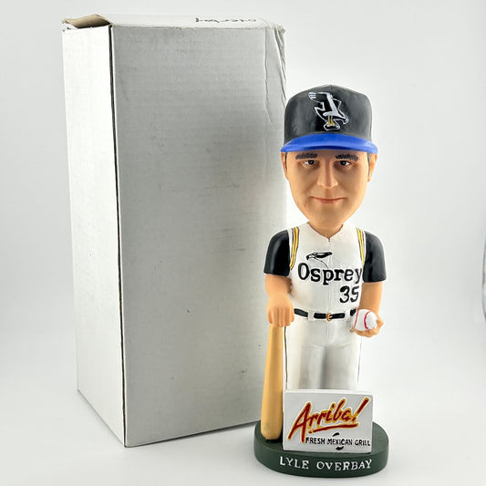 Baseball bobblehead figure with 'Osprey' uniform and 'Arriba' sign in front of a gray box.