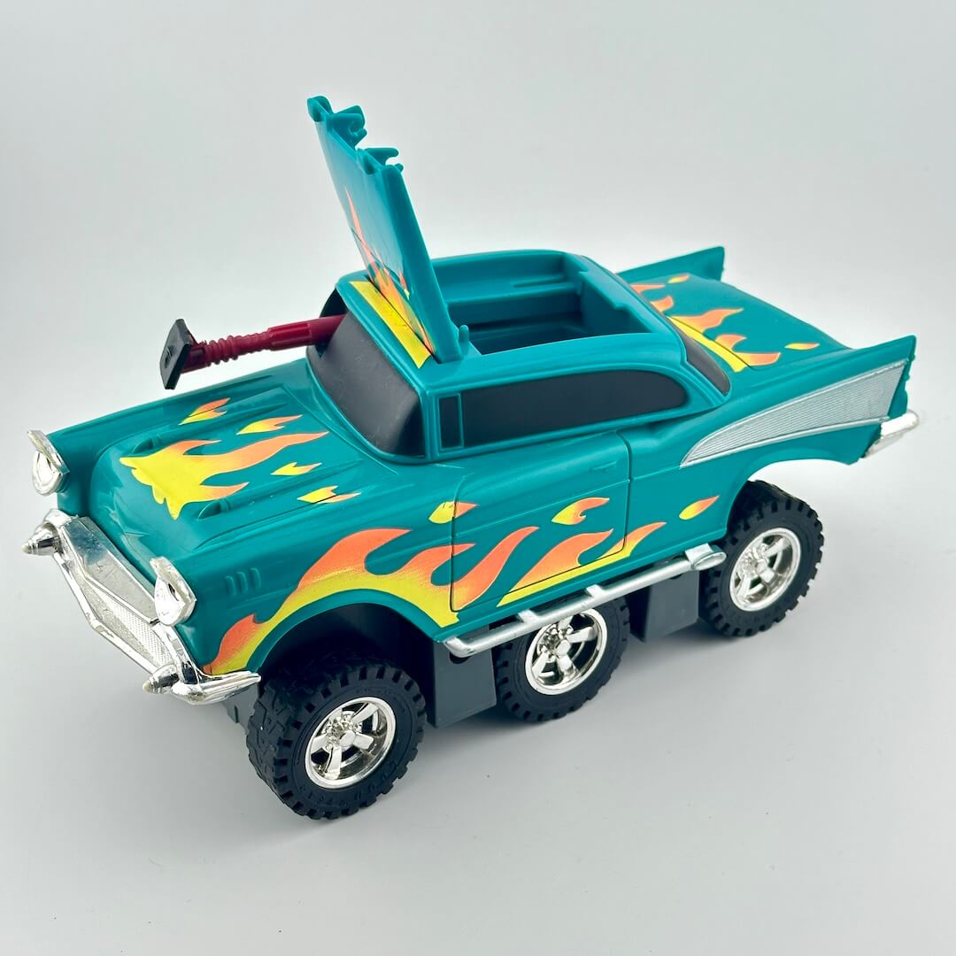 A toy hot-rod pickup truck in teal with orange and yellow flame decals, shown on a light gray studio background. 