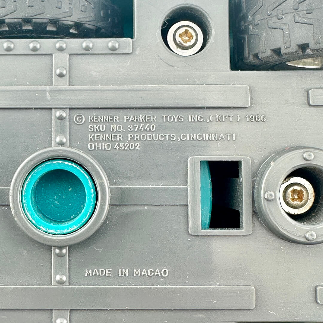 Close-up of the underside of a gray plastic toy vehicle, showing copyright and maker information embossed in plastic. 