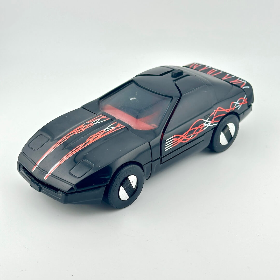 A black toy sports car with red and white flame decals, photographed on a light gray background.