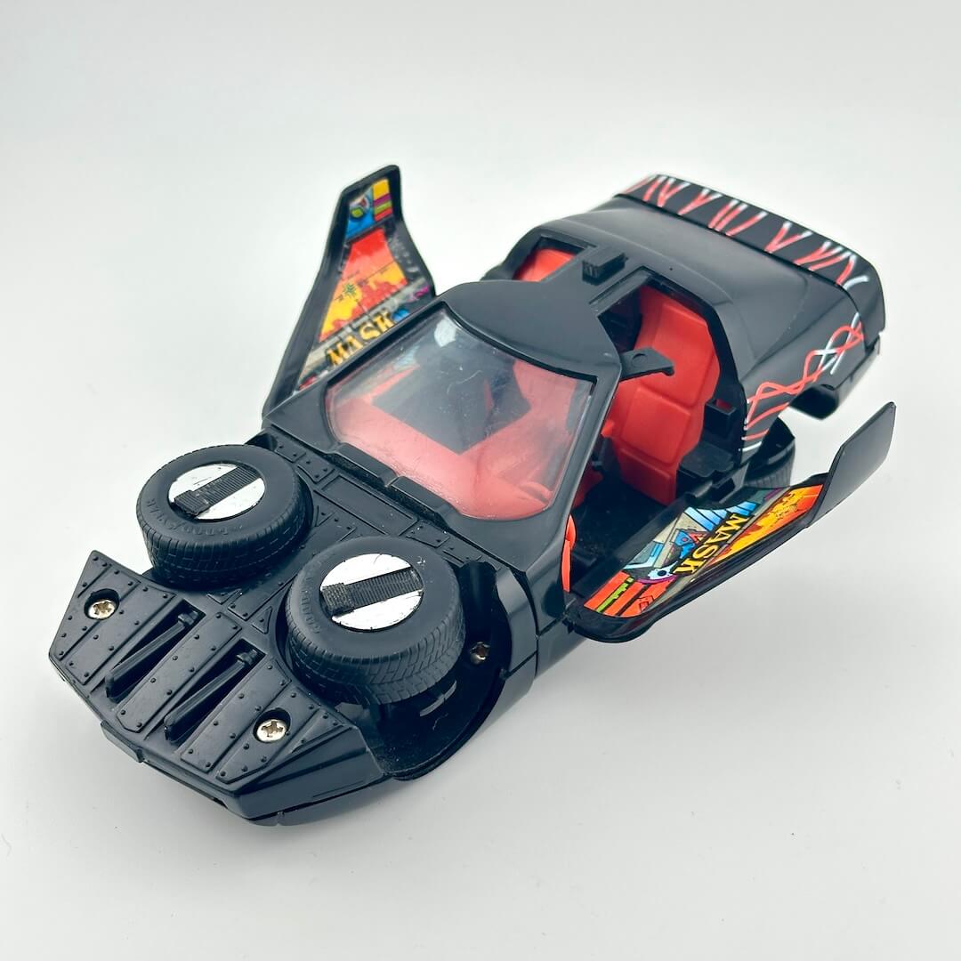 A black toy car body with red interior seats, open doors, and colorful graphic decals, photographed on a plain light background.