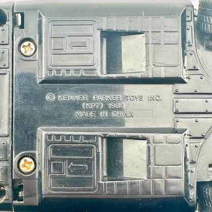 Close-up of the underside of a black plastic toy vehicle, showing molded details, screws, and embossed text.