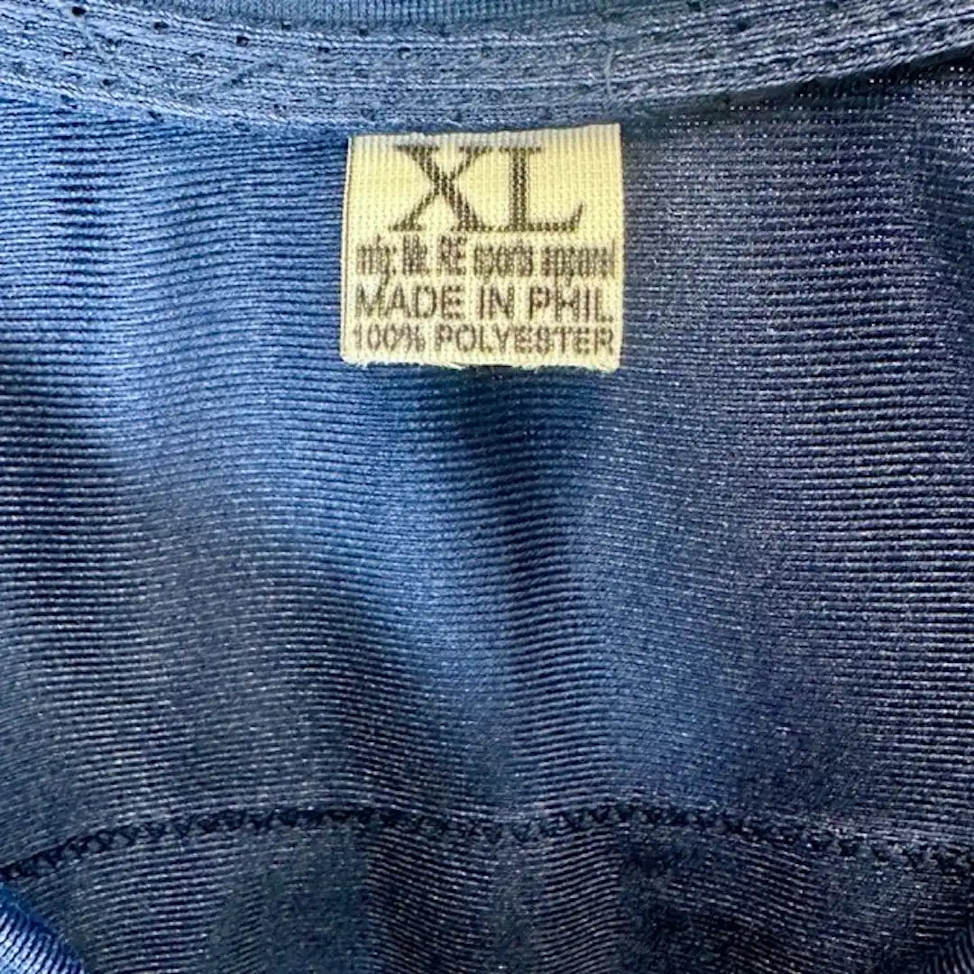 Close up of neck tag showing size XL, made in Phil, 100% Polyester. White tag, navy jersey.