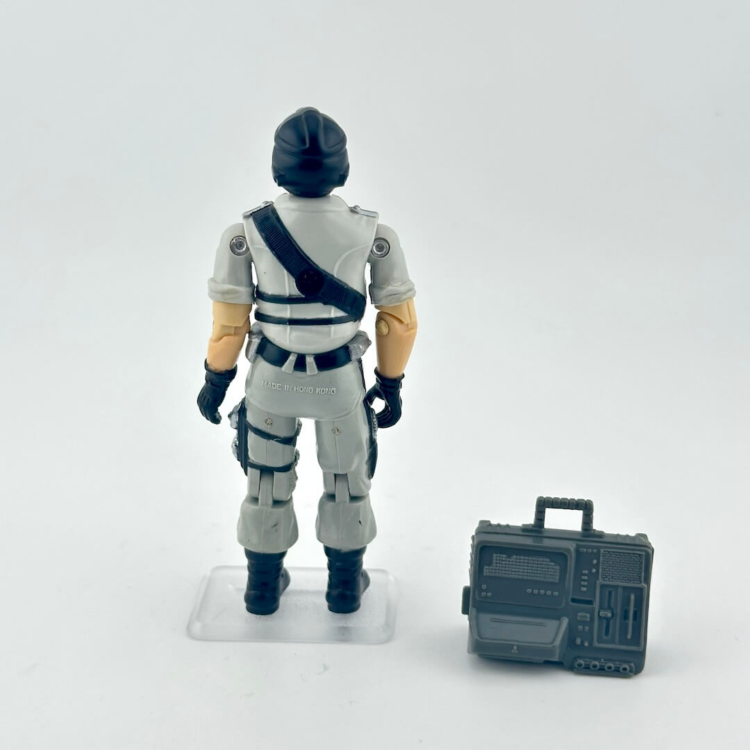 Action figure in a gray uniform with a helmet, standing next to a gray radio-like device on a white background