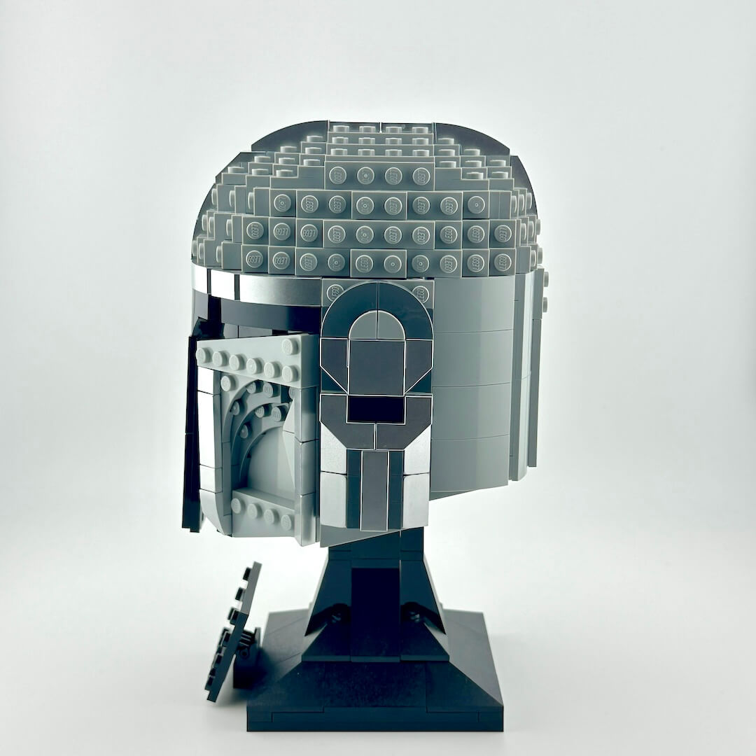 Lego Mandalorian helmet on stand against white background.
