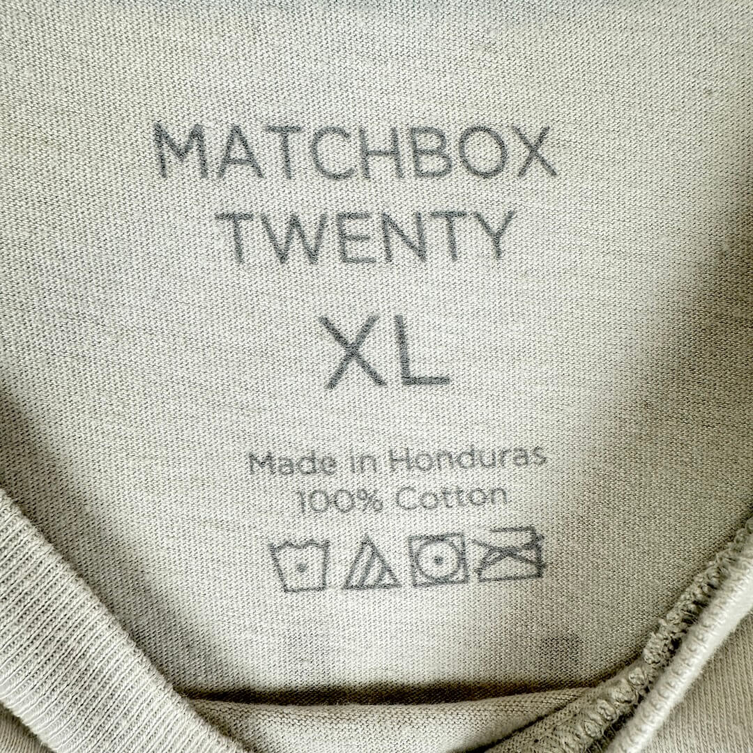 Close-up of the inner neck label of a light gray cotton garment, printed with the text 'MATCHBOX TWENTY XL'.