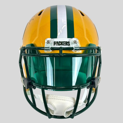 A Green Bay Packers football helmet with a gold shell, green and white stripes, a green facemask, and a clear visor.