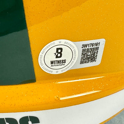 A close-up of a yellow helmet showing a circular Witness Autograph sticker and an adjacent QR code label. 