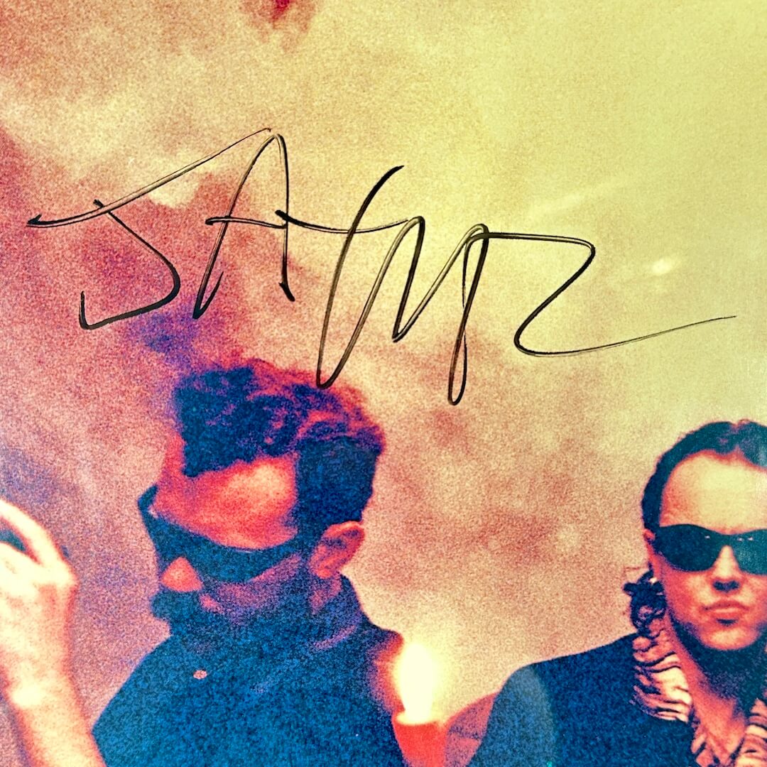 Two people with sunglasses against a colorful background with the signature. 