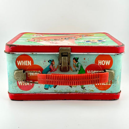 Top view of metal lunchbox showing red plastic handle and rusty latch, photographed on white background. 