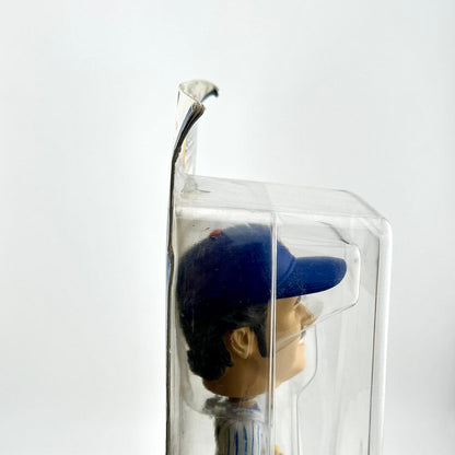 Figurine wearing a blue cap inside a clear plastic box on a white background