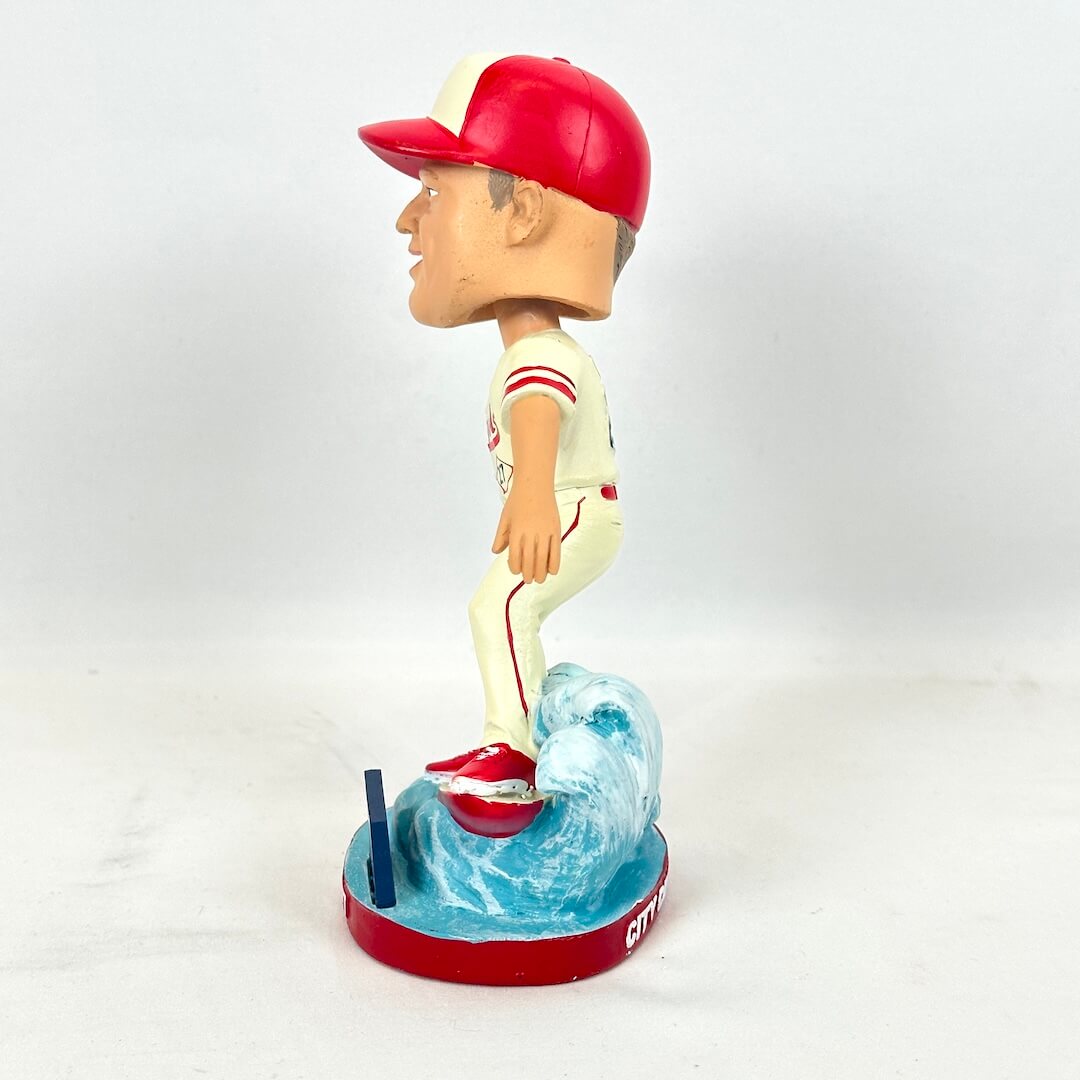 A bobblehead figurine of a baseball player in a red and white uniform and cap, standing on a blue wave-like base.