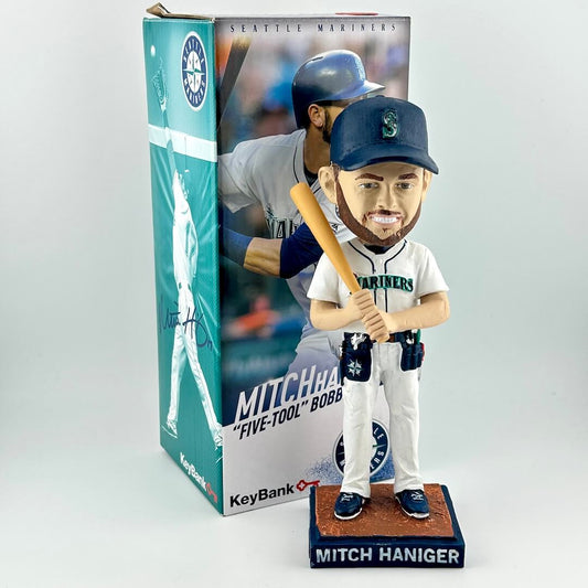 Bobblehead of baseball player in white uniform holding a bat in front of packaging on white background. 