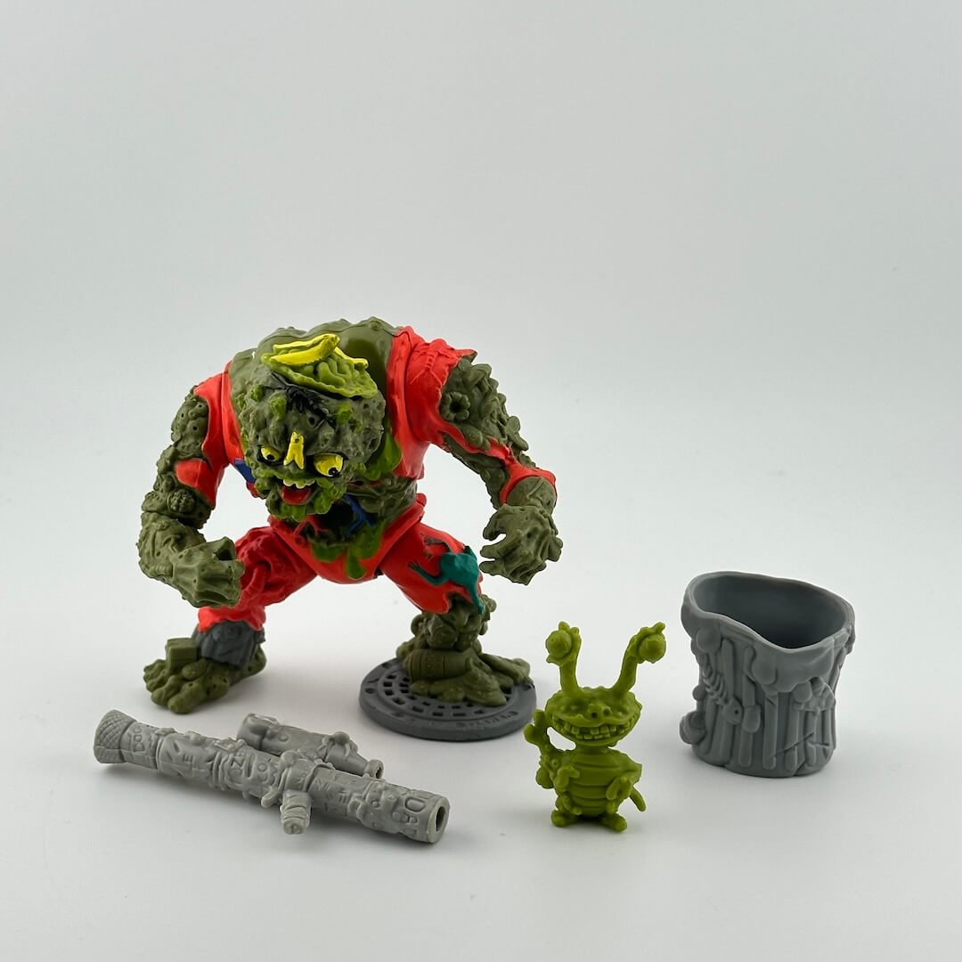 Green person with mottled, rough skin, in tattered orange jumpsuit, pictured with trash can, grey gun, and green pet.