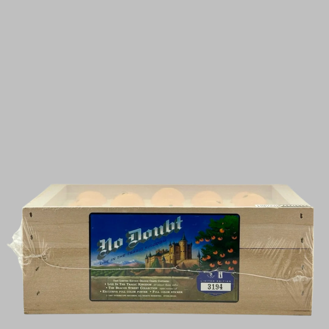 Plastic wrapped wooden fruit crate with blue label on side, & fake oranges in top. Side view.