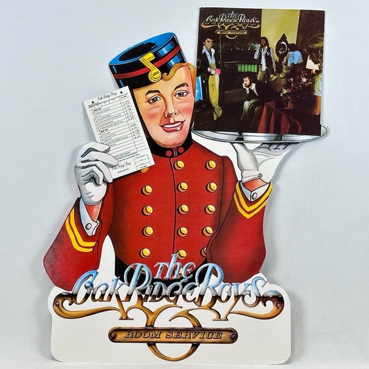 Bellhop wearing red uniform and black hat. Holding record album on plater and check in other hand. 
