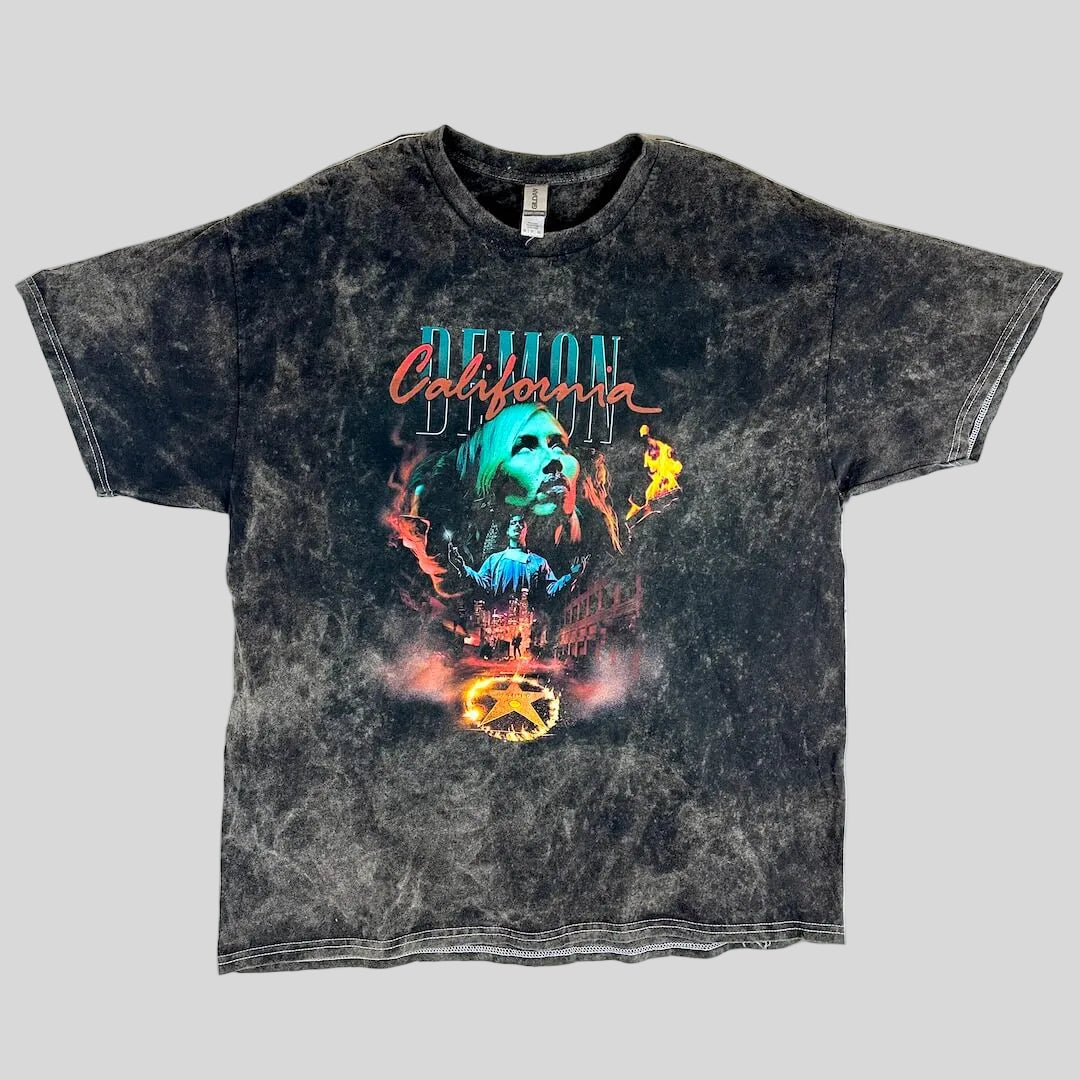 A black acid-wash graphic t-shirt featuring a central illustration of a woman's face with flames and the text 'California Demon.'