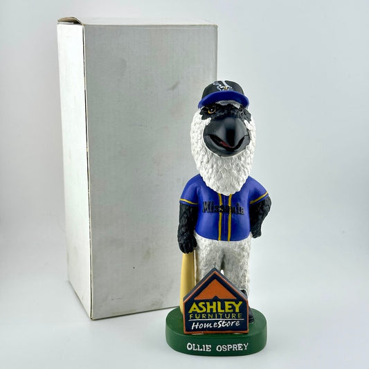 Bobblehead figure of a bird in a blue uniform with a hat, standing next to a branded box on a light gray background.