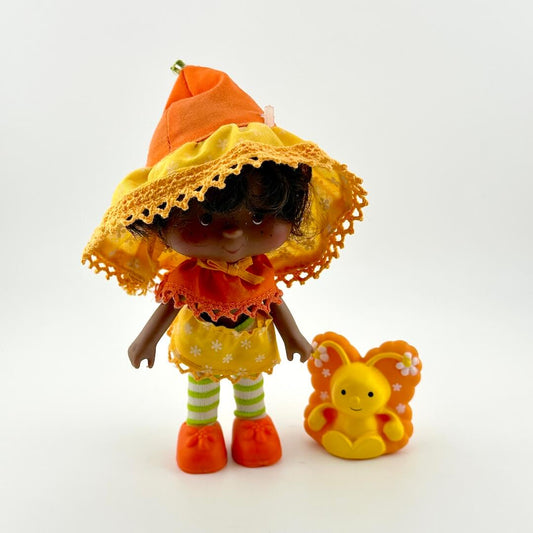 Toy doll in orange and yellow outfit next to orange and yellow butterfly. 