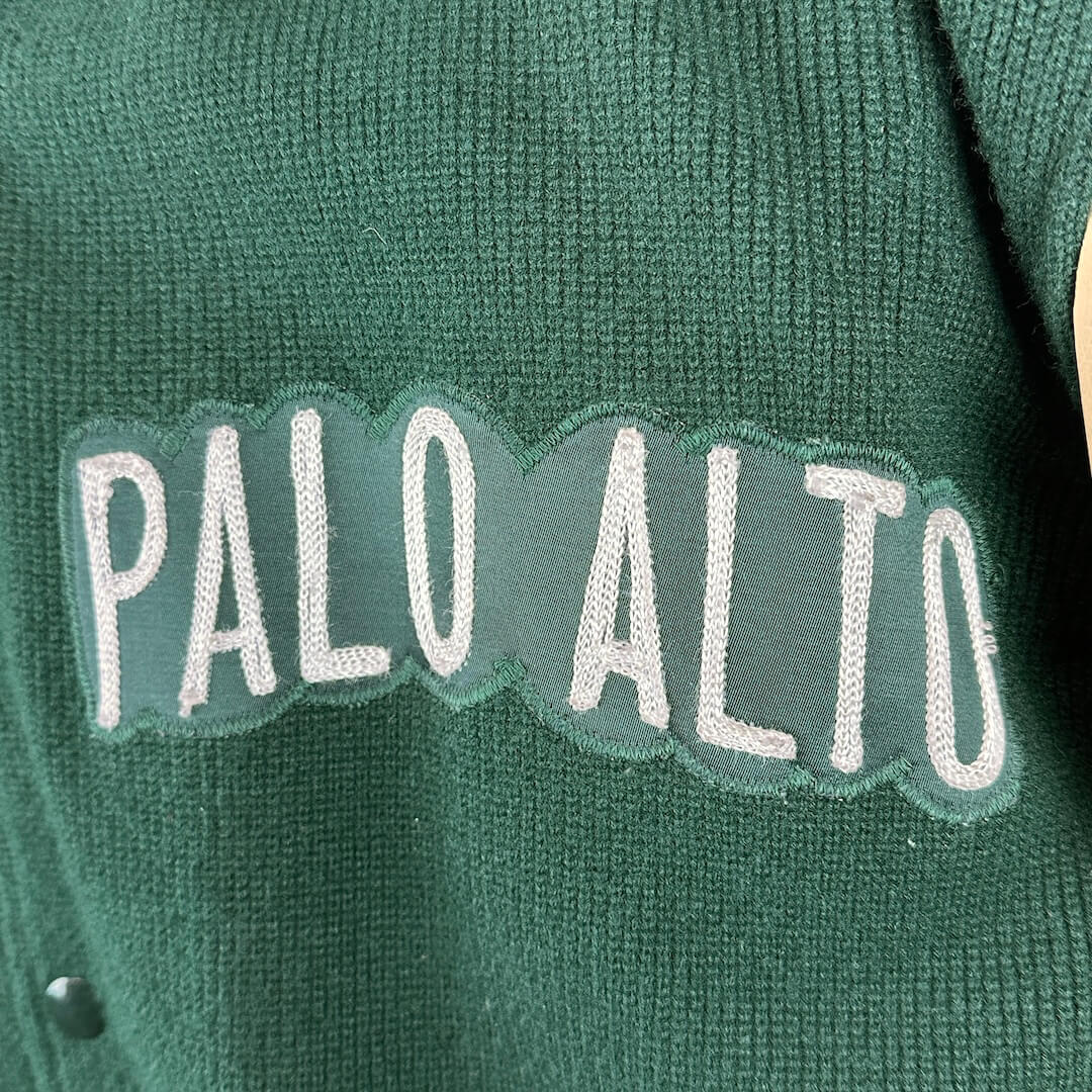 Green sweater with 'PALO ALTO' text on a close-up of fabric texture.