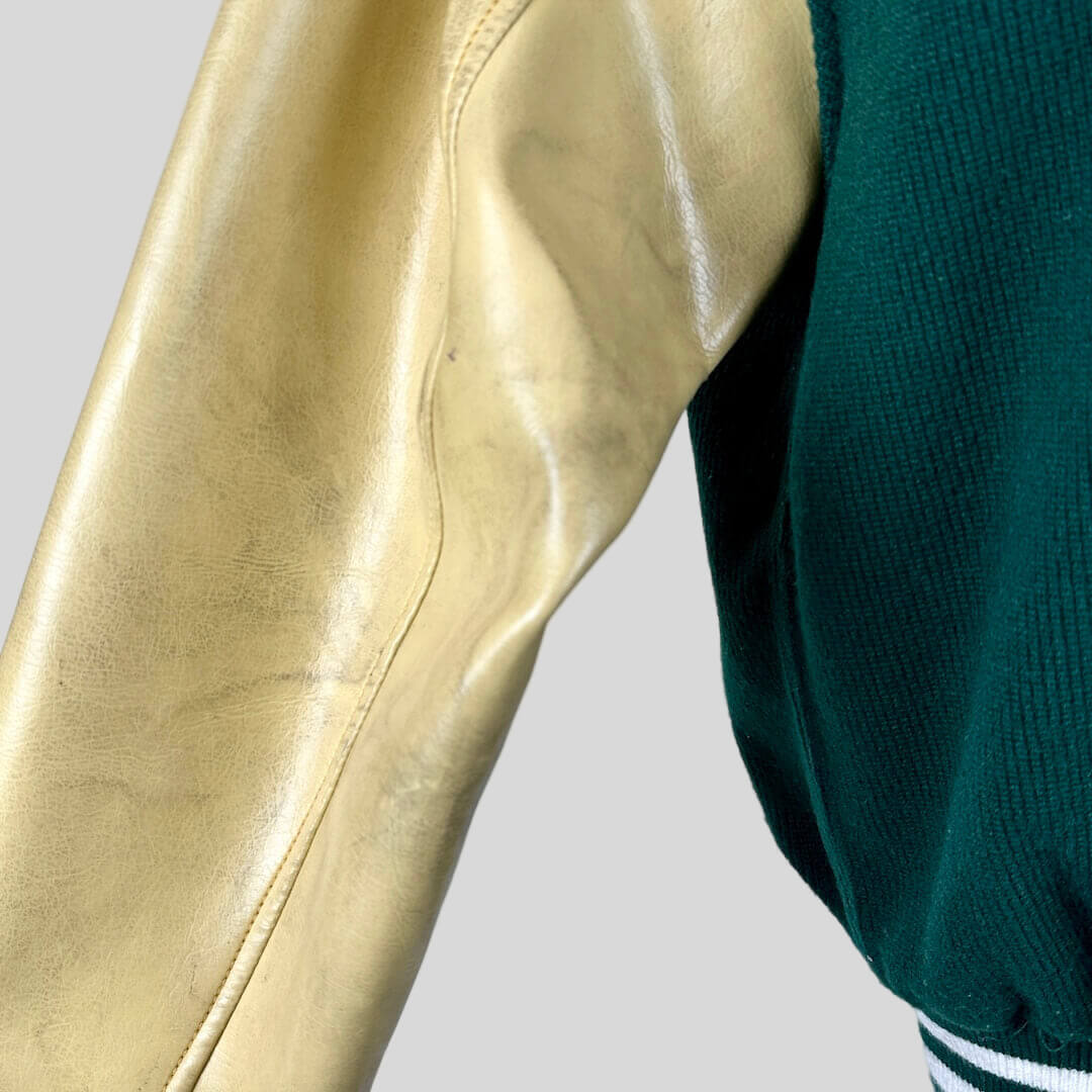 Close-up of a beige leather jacket sleeve and green sweater sleeve against a light blue background