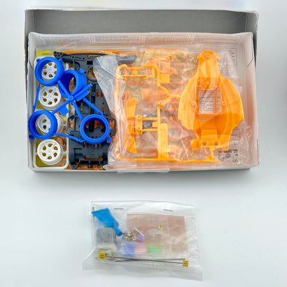 A car model kit parts set in its original box, featuring bright orange body panels, blue wheels, and various accessories.
