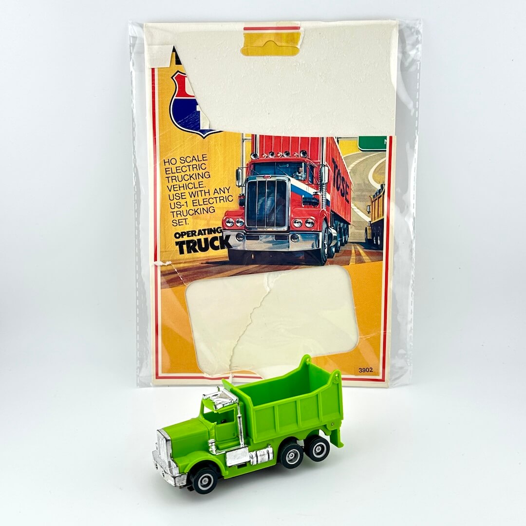 Green toy truck in front of its packaging on a white background